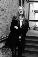 Black and white photo. Beautiful young blonde woman walking on the street. Dressed in a black coat and a warm knit sweater.