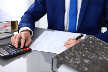 Close up view of bookkeeper or financial inspector hands making report, calculating or checking balance. Internal Revenue Service inspector checking financial document.