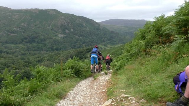 Group of three mountain bicycle riders riding down the trail in Lake District, England.