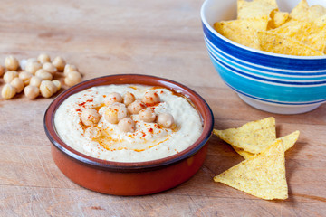 Houmous dip topped with paprika and chickpeas in  terracotta dish served with tortilla chips