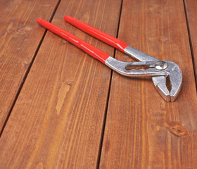 Metal plumber wrench with red handles on wooden surface