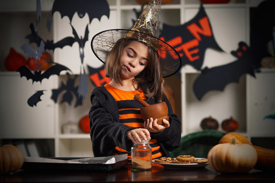 Cute little girl in a Halloween costume is preparing cookies for Trick or Treat
