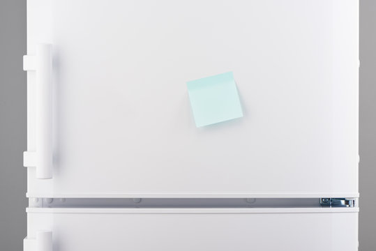 Blank light blue sticky paper note on white refrigerator