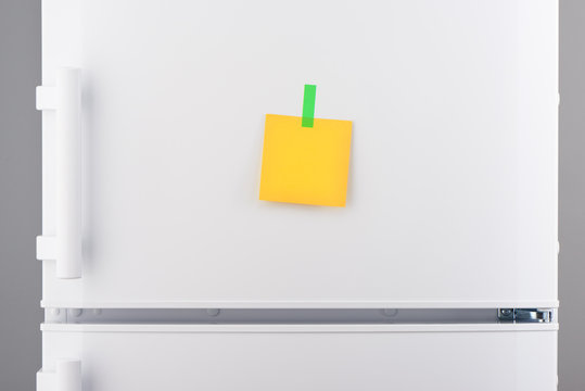 Blank yellow paper note and green sticker on white refrigerator