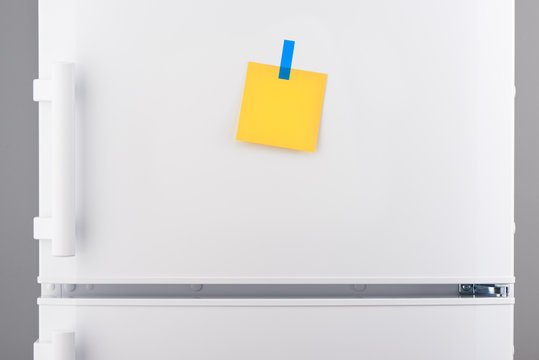 Blank yellow paper note and blue sticker on white refrigerator