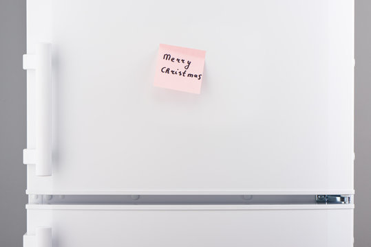 Merry Christmas note on pink sticky paper on white refrigerator