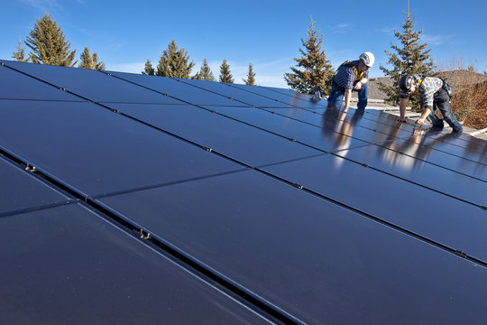 Two solar panel installers install solar panels on roof, Alberta foothills near Black Diamond, Alberta, Canada.