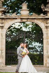 Obraz premium Handsome groom hugging beautiful bride with bouquet in romantic european park