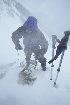 A climber belaying an ice route in fierce snow conditions on the Lone Ranger WI 3, Kananaskis Country, Rocky Mountains, Alberta, Canada