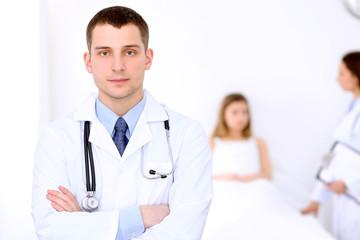 Friendly male doctor on the background with patient in the bed