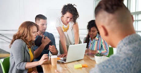Multi ethnic group of succesful creative business people using a laptop during candid meeting