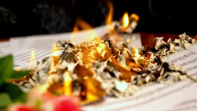 Sheet music are burning on background of girl playing violin. Girl composes music. Camera moves from right to left. 4k.