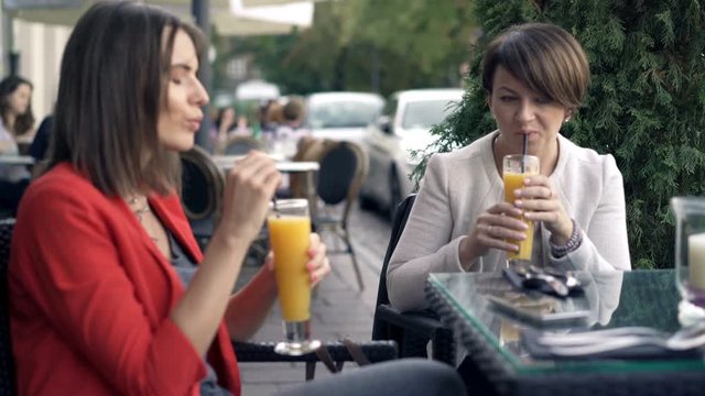 Two beautiful girlfriends chatting, laughing and drinking in cafe in the city, 4K 
