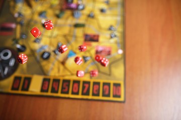 Several rolling red dice fall on a table with boardgame. Gameplay moments