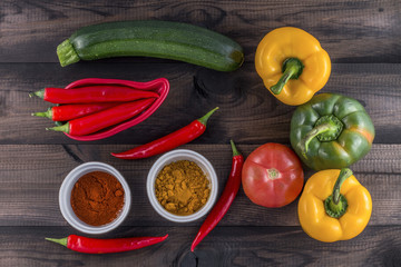 green and yellow paprika with tomato, zucchini and chilli powder on wooden background