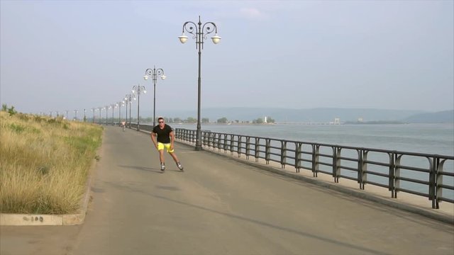 Young sporty man roller skating on summer waterfront HD