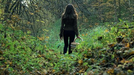 Slender young woman in a brown jacket walking through the forest holding basket