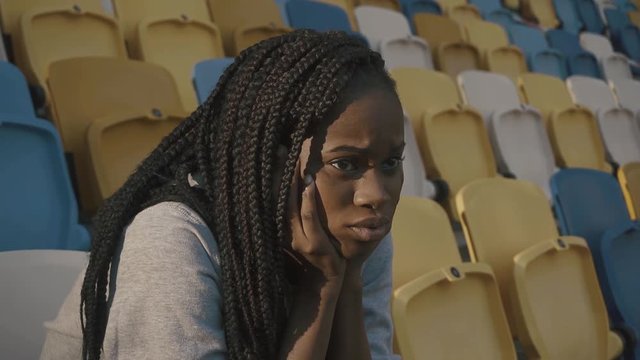 Young african american girl sitting on tribune and looking the match