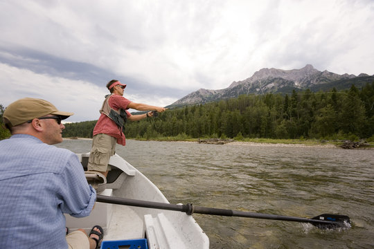 Young men fly fishing on the Elk River from a dory while guide watches, Fernie, East Kootenays, British Columbia, Canada.