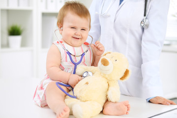 Happy cute baby  at health exam at doctor's office. Toddler girl is sitting and keeping stethoscope and teddy bear