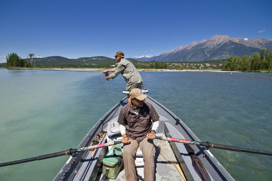 Middle-aged man fly-fishing on Kootenay river with guide rowing fishing boat, East Kootenays, BC, Canada.