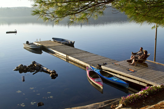 Middle-aged couple enjoy quiet morning on dock near their cottage, Source Lake, Algonquin Park, Ontario, Canada.