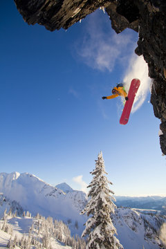 A male snowboarder  catches some off a cliff on his splitboard in the Revelstoke Mountain Resort Backcountry, Revelstoke, BC