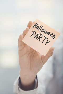Woman holding adhesive note with Halloween party text