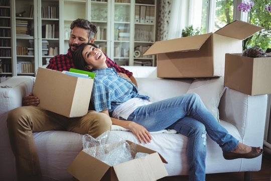 Couple relaxing on sofa while unpacking carton boxes