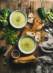 Two bowls of homemade pea, broccoli and zucchini cream soup served with fresh baguette and...
