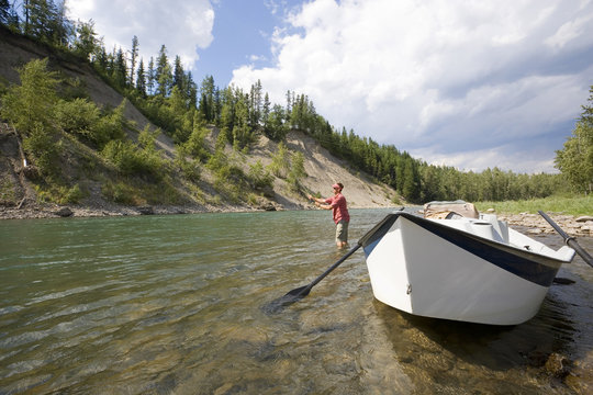 Young man fly fishing on the Elk River from a dory, Fernie, East Kootenays, British Columbia, Canada.
