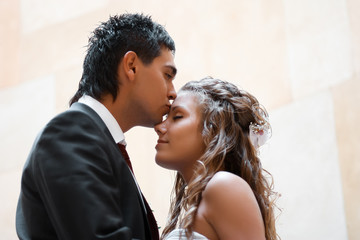 Brunette groom kisses bride's forehead tender while she leans to