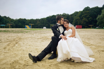Fototapeta na wymiar Kissing wedding couple sits on the beach surround with green tre