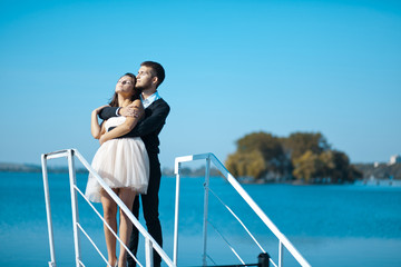 Man in black hugs tender lady in short white dress while