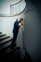 Fototapeta premium Bride leans to the white wall while groom kisses her neck with p