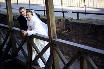 Young smiling wedding couple bends over the wooden handrails whi