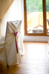 Chair covered with white silk and decorated with dark pink ribbo
