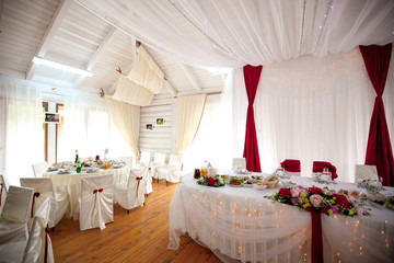 Dinner tables decorated with white and red cloth stand in wooden