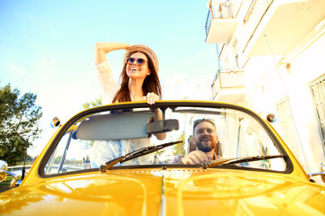 Happy to travel together. Joyful young couple smiling while riding in onvertible - obrazy, fototapety, plakaty