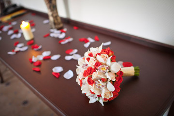 Wedding bouquet made of lilies and red roses lies on the wooden