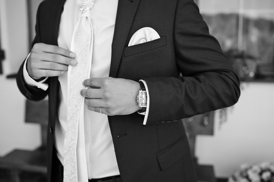 Close-up of man's hands holding white bow tie on the shirt