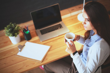 Fototapeta na wymiar Portrait of relaxed young woman sitting at her desk holding cup of coffee