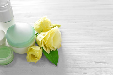 Cosmetic bottles and eustoma flowers on light wooden background