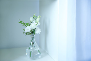 Beautiful eustoma flowers in glass vase on white shelf