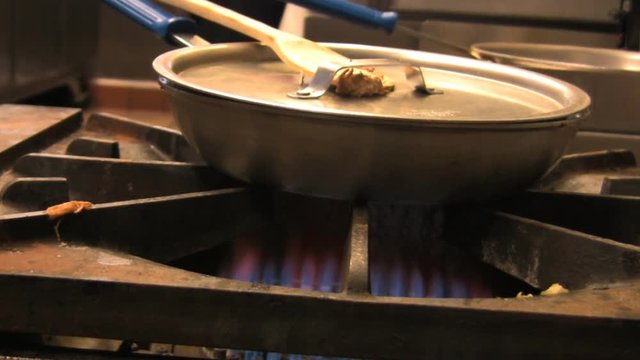 A frying pan with lid on top of an industrial gas burner cooking food. HD 1080p.