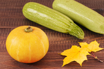 Pumpkin and zucchini on wooden table with autumn leaves