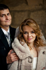 Groom holds shoulders of beautiful bride enveloped in winter coa