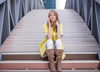 cheerful beautiful woman sitting on the stairs and talking on the bridge