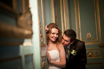 Bride leans to the old wall while groom kisses her shoulder tend