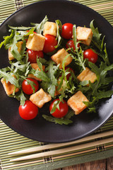 Salad: fried tofu with tomatoes and fresh arugula close-up on a plate. vertical top view
